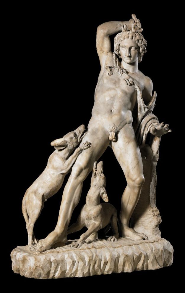 Sculpture. A muscular, nude man plants his feet widely and leans back from two dogs that jump up on and crouch under his forward leg. A cape hands loosely around his neck and one shoulder, and drapes over one arm. 